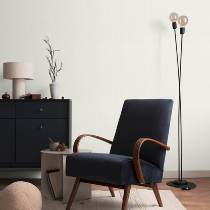 Mid-century navy armchair with curved wood arms and legs, beside a white side table; double-globe floor lamp and dresser.