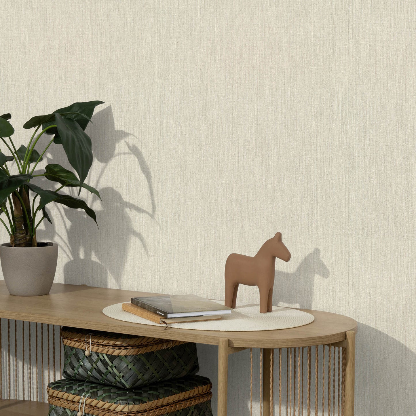 Wooden console table with a potted plant, beige horse figurine, round mat, a book, and woven baskets below.