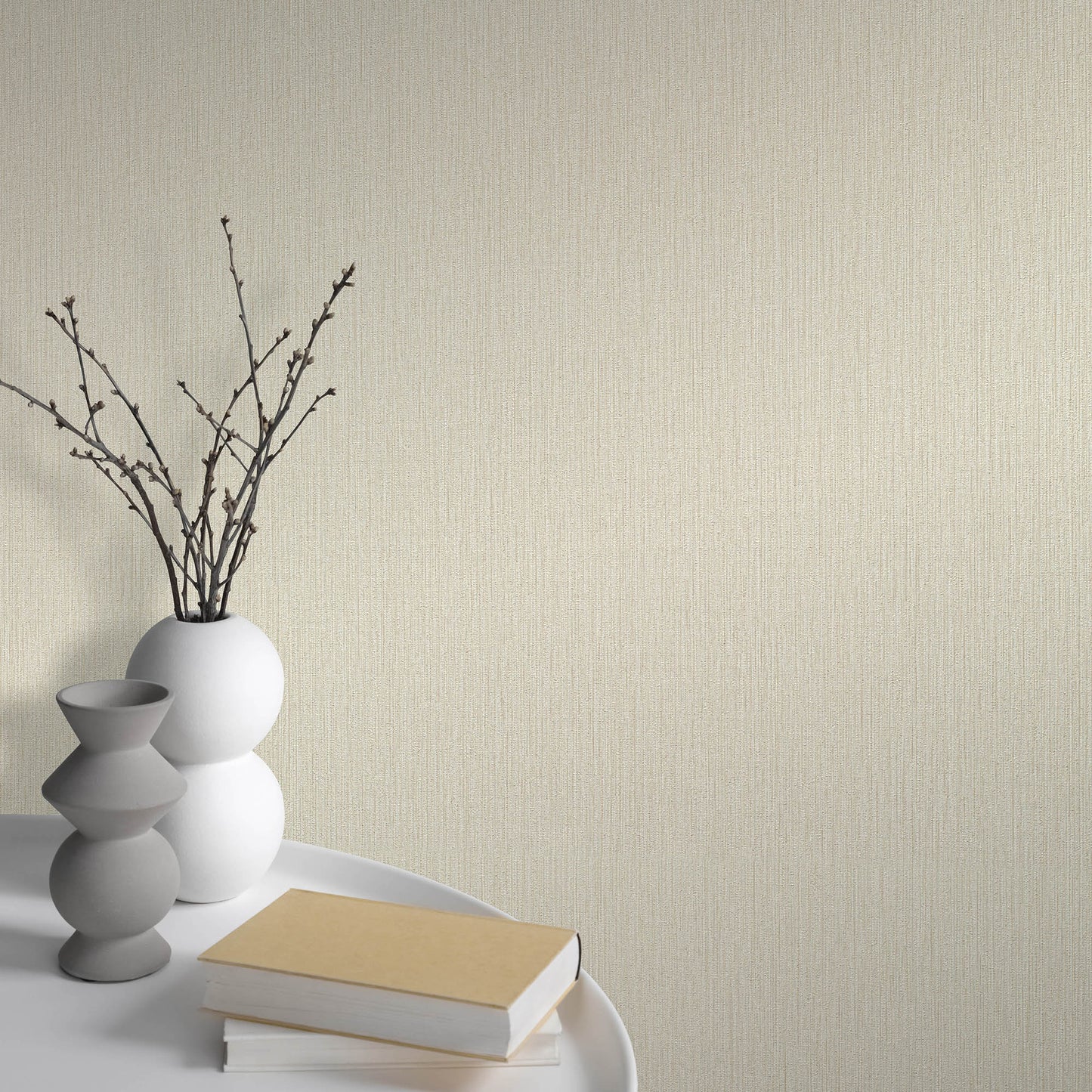 Minimalist white spherical vase with bare branches beside stacked gray ceramic vases and beige books on a white tray.