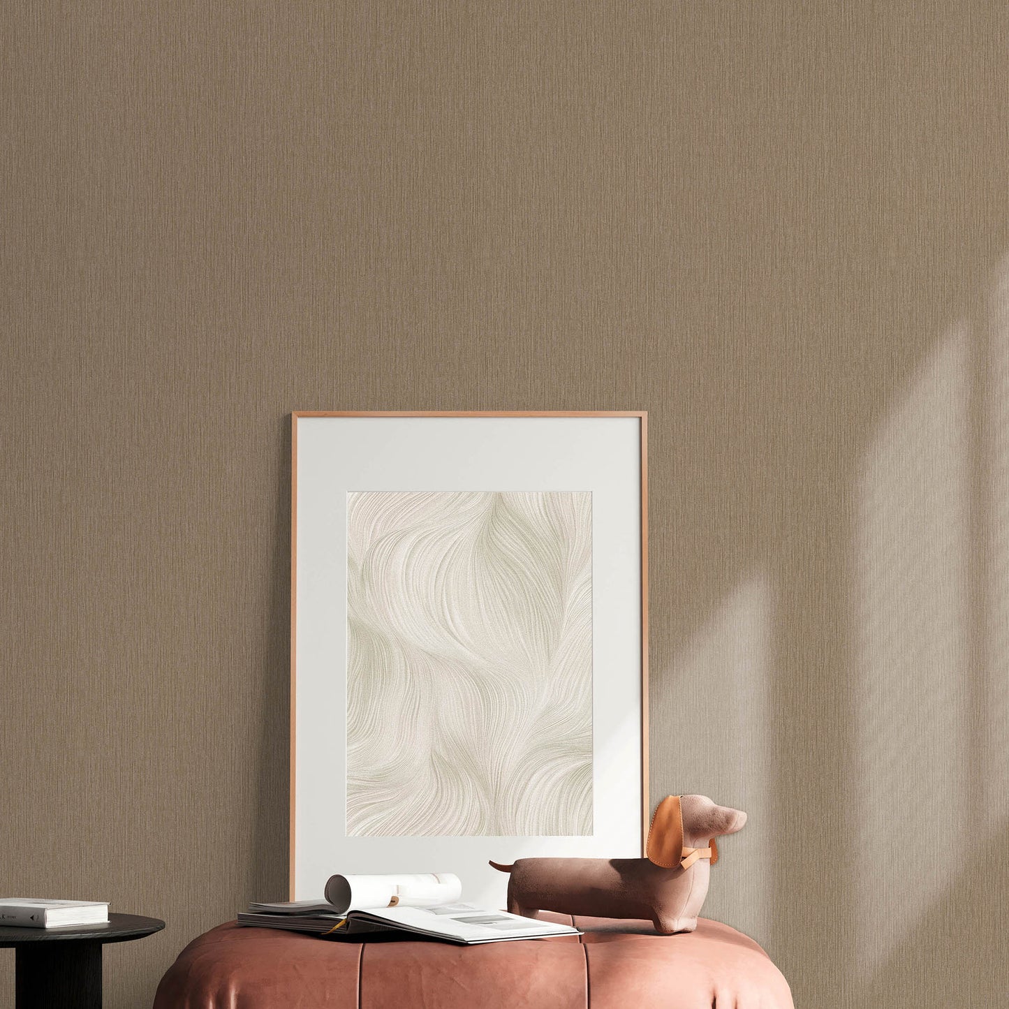 Beige room with a rose-gold framed abstract swirl art leaning on the floor, pink ottoman, brown dachshund plush & magazines.