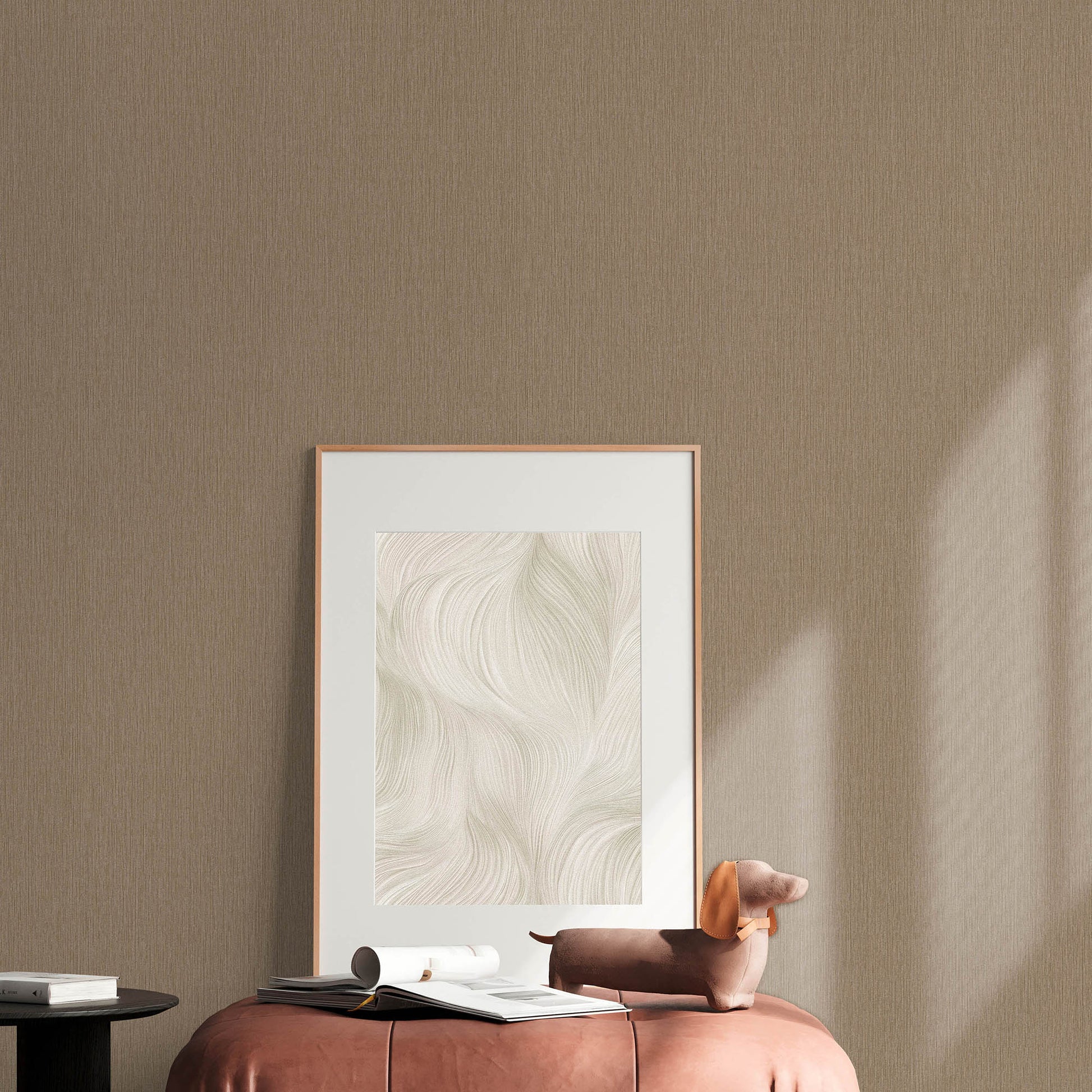 Beige room with a rose-gold framed abstract swirl art leaning on the floor, pink ottoman, brown dachshund plush & magazines.