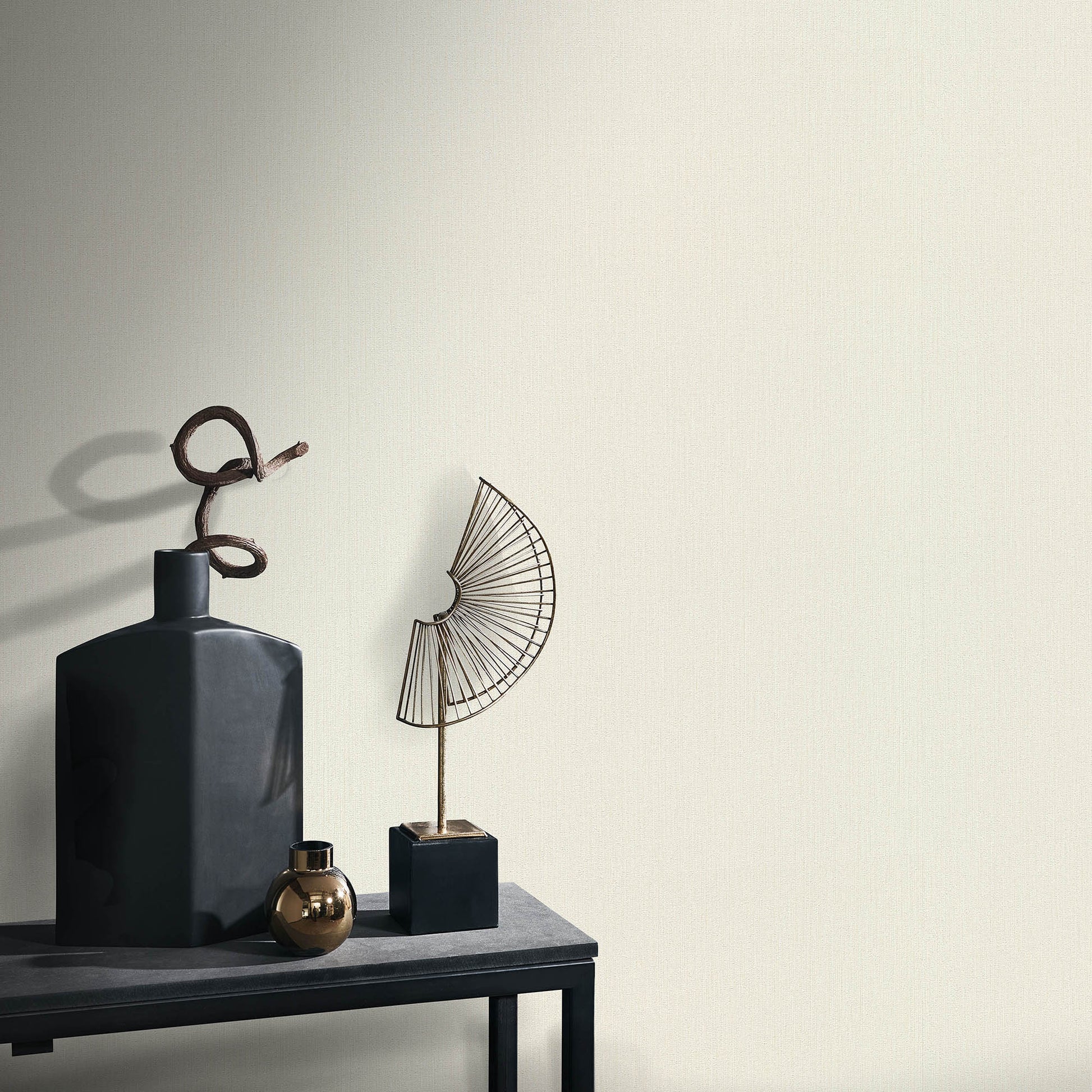 Matte charcoal bottle with looped rope, brass orb, and a wire fan sculpture on a dark shelf—minimalist decor.