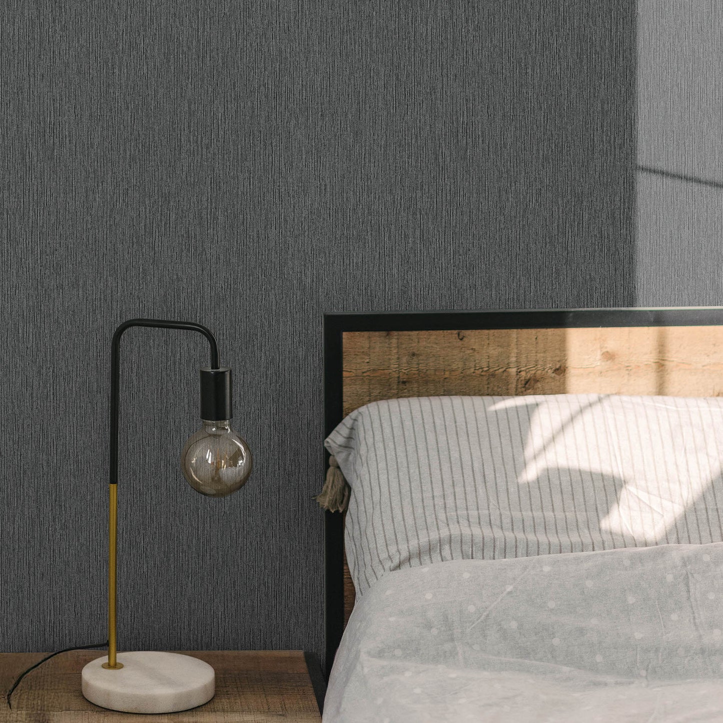 Modern arc table lamp with black & yellow stem, visible bulb, white marble base on wooden nightstand beside gray striped bed.