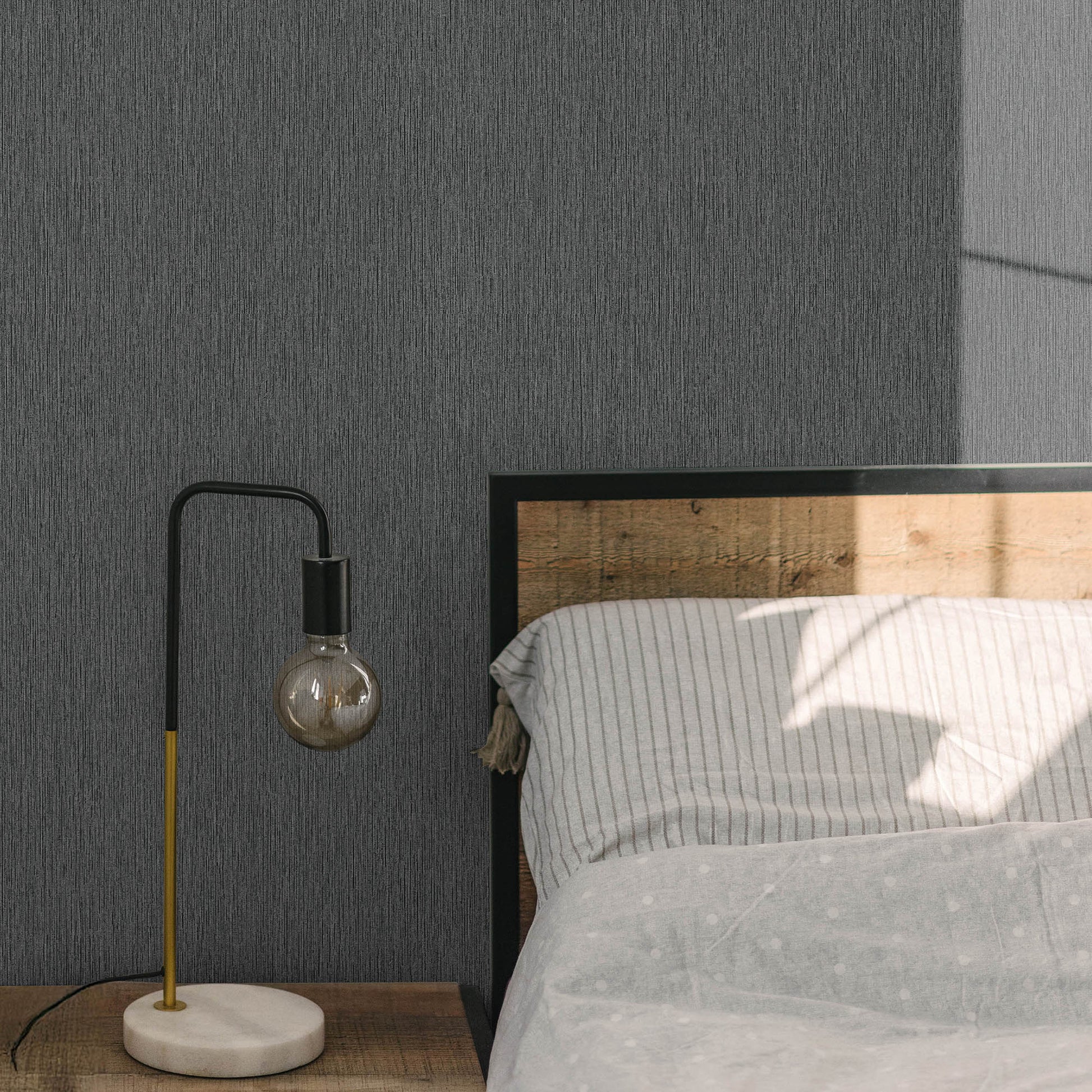 Modern arc table lamp with black & yellow stem, visible bulb, white marble base on wooden nightstand beside gray striped bed.