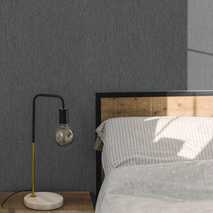Modern arc table lamp with black & yellow stem, visible bulb, white marble base on wooden nightstand beside gray striped bed.