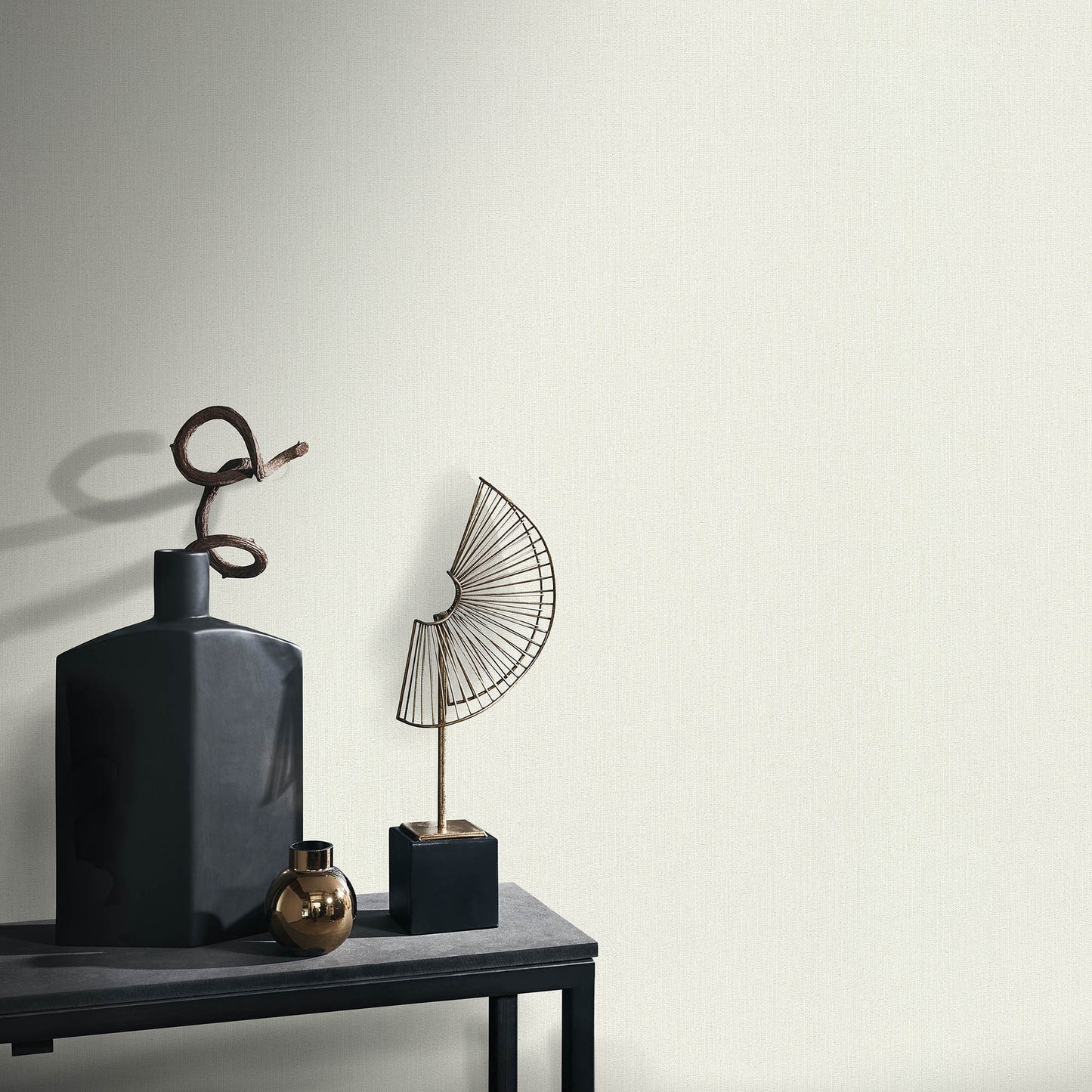 Dark matte ceramic bottle vase with looped twig, bronze orb, and geometric wire fan sculpture on a black pedestal table.