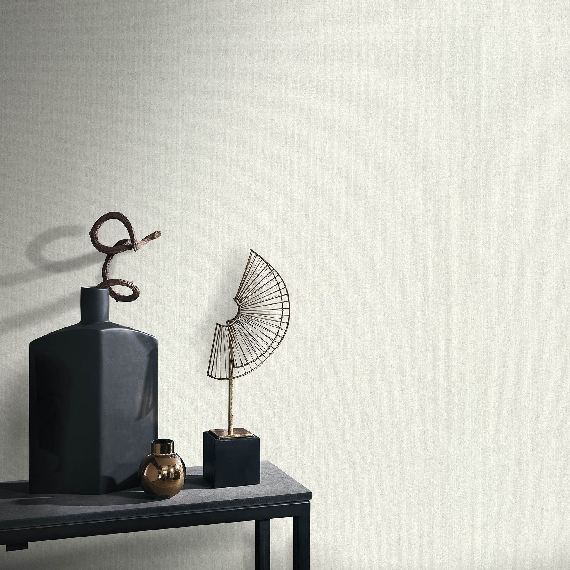 Dark matte ceramic bottle vase with looped twig, bronze orb, and geometric wire fan sculpture on a black pedestal table.