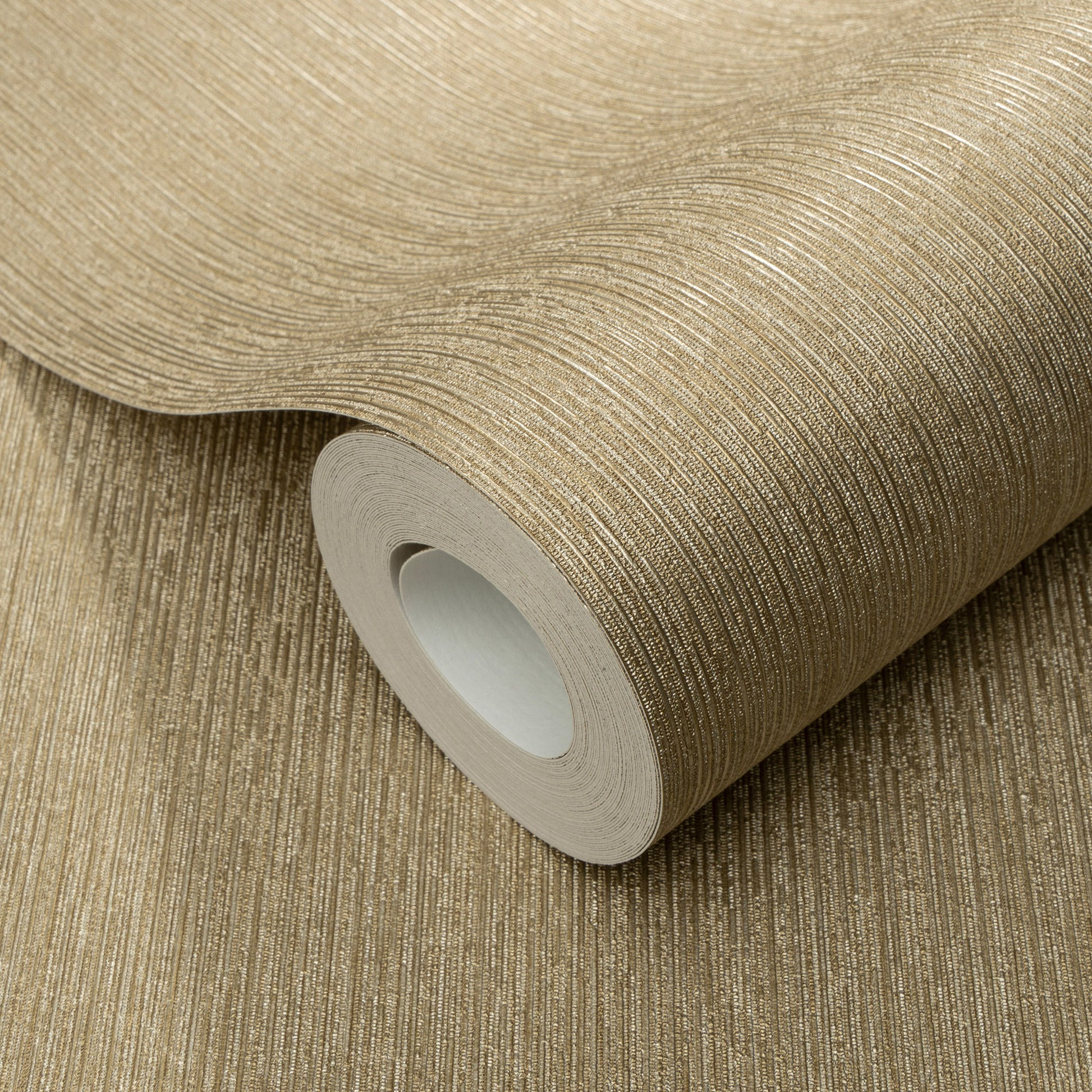 Gold metallic wallpaper roll with fine ribbed texture and shimmering stripes; curved roll with white cardboard core.