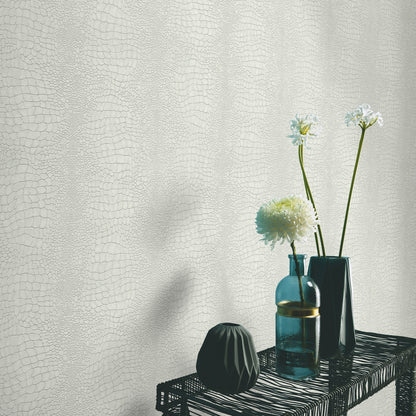 Beige textured backdrop with a black woven shelf holding two teal glass bottles, a faceted black vase, and white blooms.