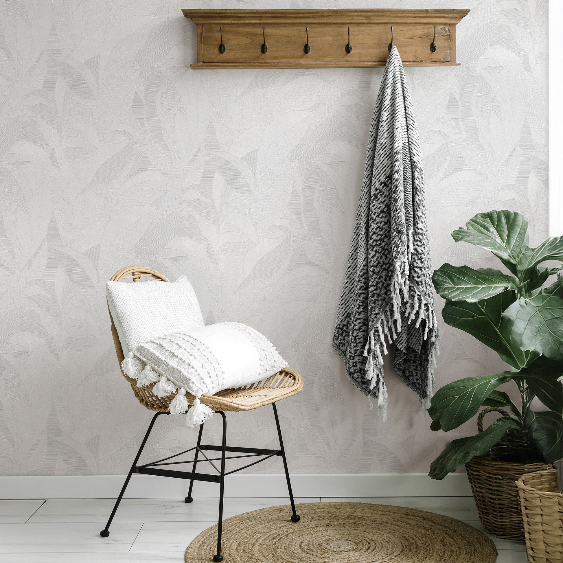Natural wicker chair with white tassel pillow and gray striped throw, wall-mounted wooden rack, large green plant in basket, round jute rug.