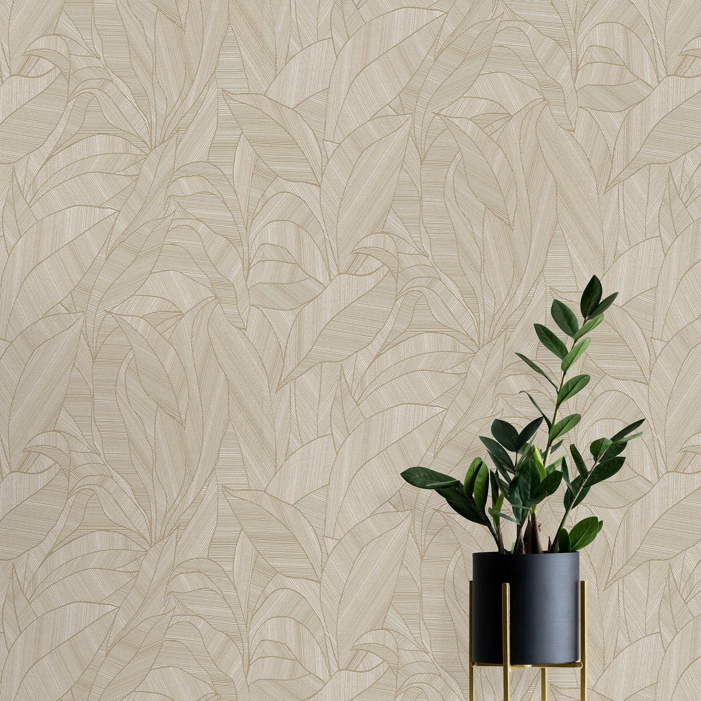Beige tropical leaf wallpaper backdrop with a dark gray planter featuring gold accents and a tall glossy green plant.