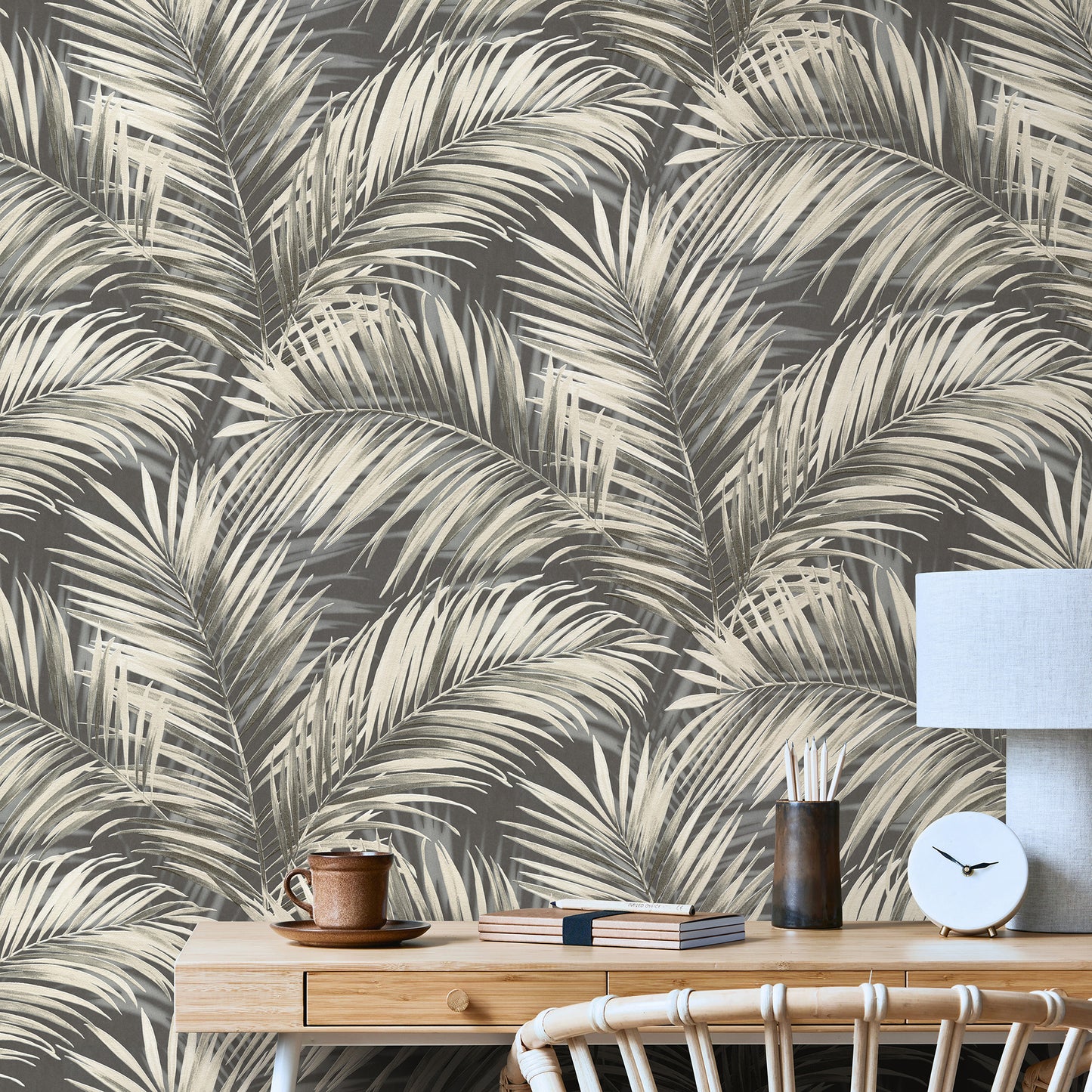 Black palm-leaf wallpaper in a room with a light wood sideboard, mug, books, dark vase, blue lampshade and clock.