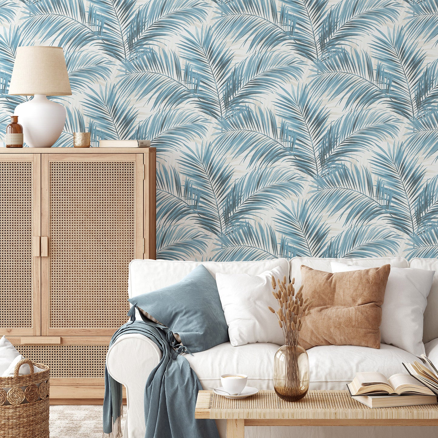Blue palm-leaf wallpaper in teal and white, shown in a cozy living room with light wood cabinet and white sofa.