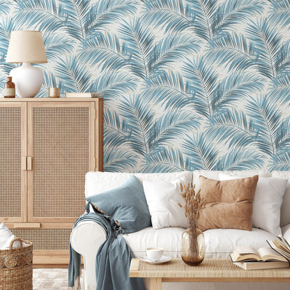 Blue palm-leaf wallpaper in teal and white, shown in a cozy living room with light wood cabinet and white sofa.
