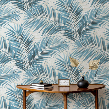 Mid-century oval wooden console table beside blue palm-leaf wallpaper; books, clock, and black vase with golden palm fronds.