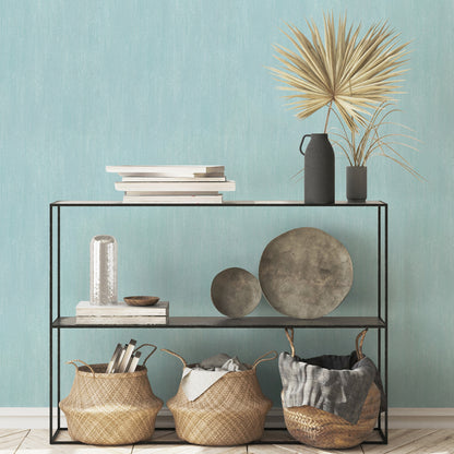 Blue raised-texture wallpaper on the wall; foreground features a black metal shelf & stacked books, black vases with dried palm, decorative stone plates & woven baskets.