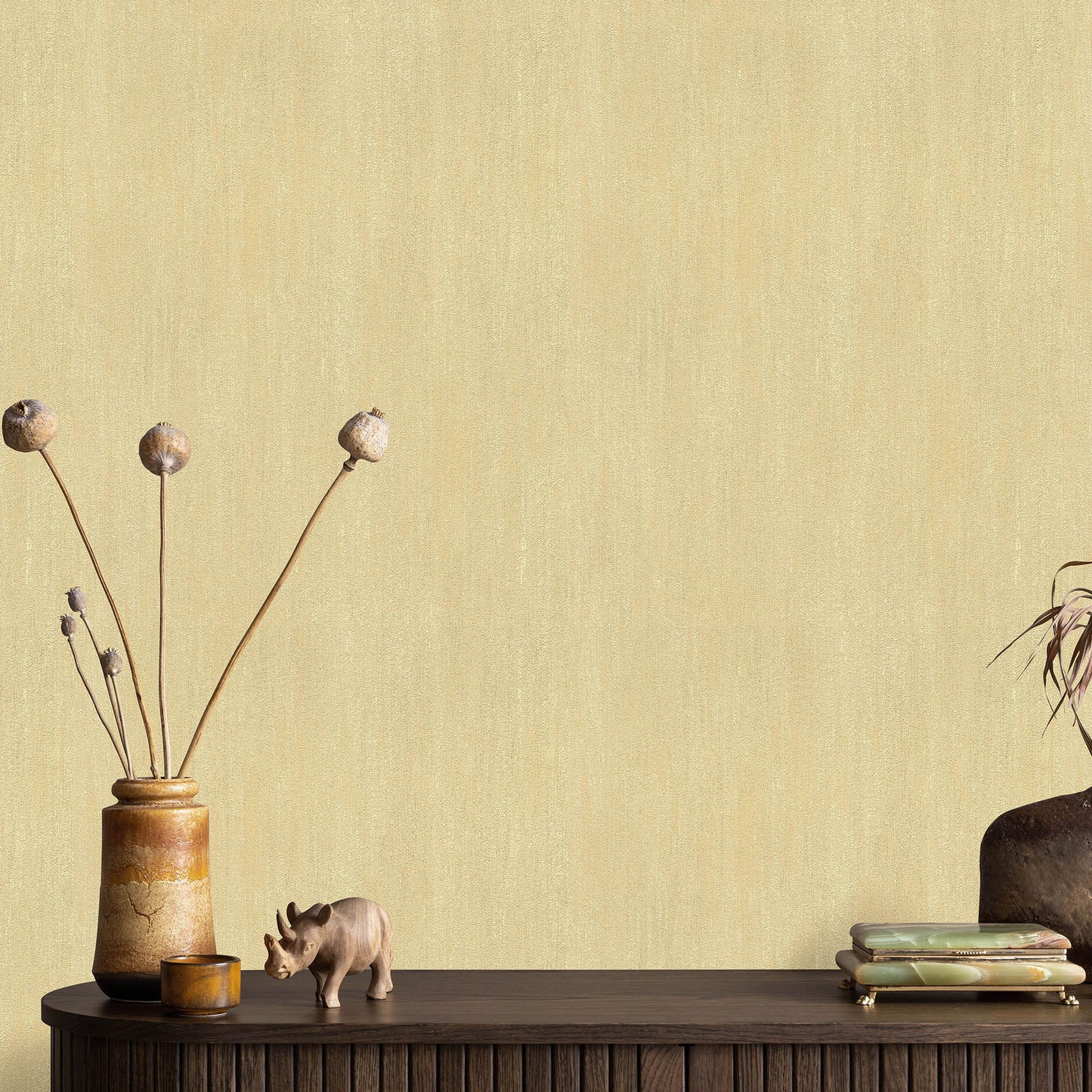 Beige sepia wallpaper with raised texture serves as backdrop for a dark wooden table displaying a ceramic vase with tall dried stems, a small hippo figurine, a stack of books & a plant.