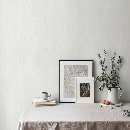 Neutral still life with two framed artworks, a white ceramic pitcher with greenery, a mug and books on beige linen table.
