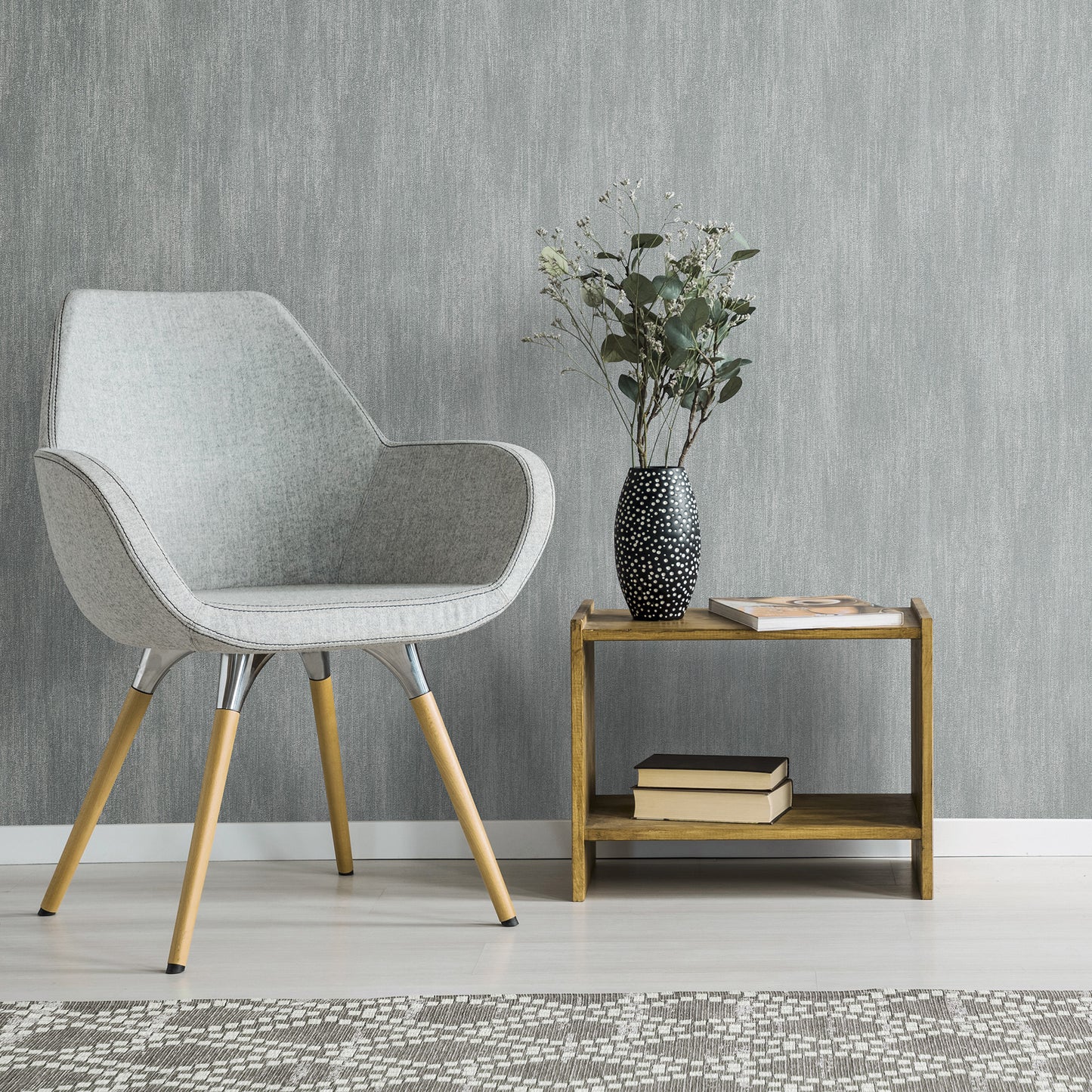 Light gray mid-century armchair with wooden legs beside a two-tier wooden side table, vase with greenery and books.