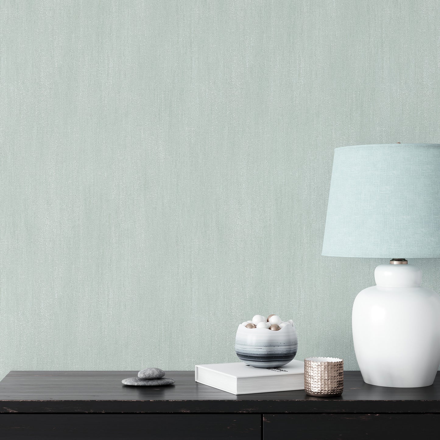 White ceramic table lamp with pale blue shade on dark wood console, beside books, stone bowl & woven candle holder.