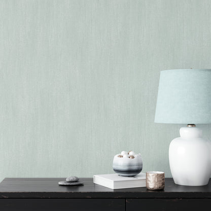 White ceramic table lamp with pale blue shade on dark wood console, beside books, stone bowl & woven candle holder.