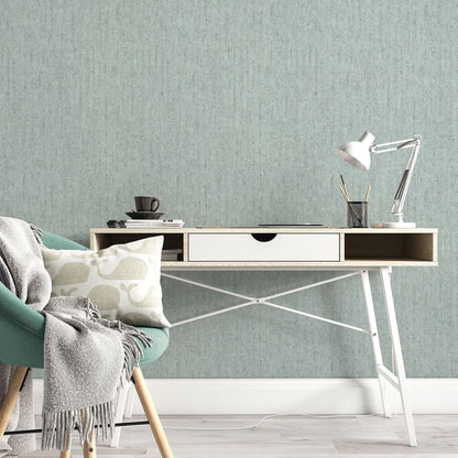 Teal upholstered chair beside a light wood desk with white drawer, silver desk lamp, mug, pencils, books, gray throw.