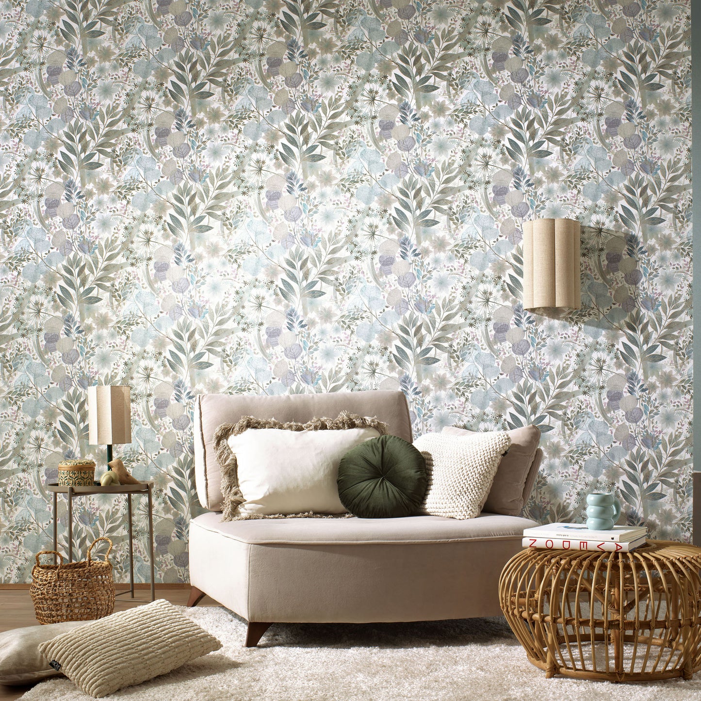 Blue floral wallpaper with a botanical pattern in sage, blue and beige; boho living room with a beige sofa, cushions, and a woven rattan coffee table.