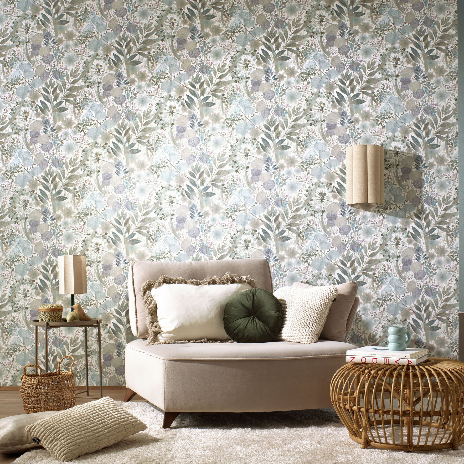 Blue floral wallpaper with a botanical pattern in sage, blue and beige; boho living room with a beige sofa, cushions, and a woven rattan coffee table.