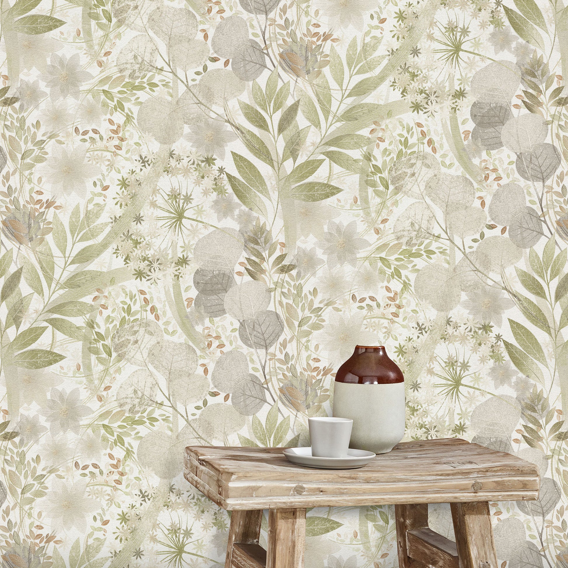 Botanical wallpaper in sage, beige and gray tones with leafy motifs; rustic wooden table holding a brown bottle and white cup.