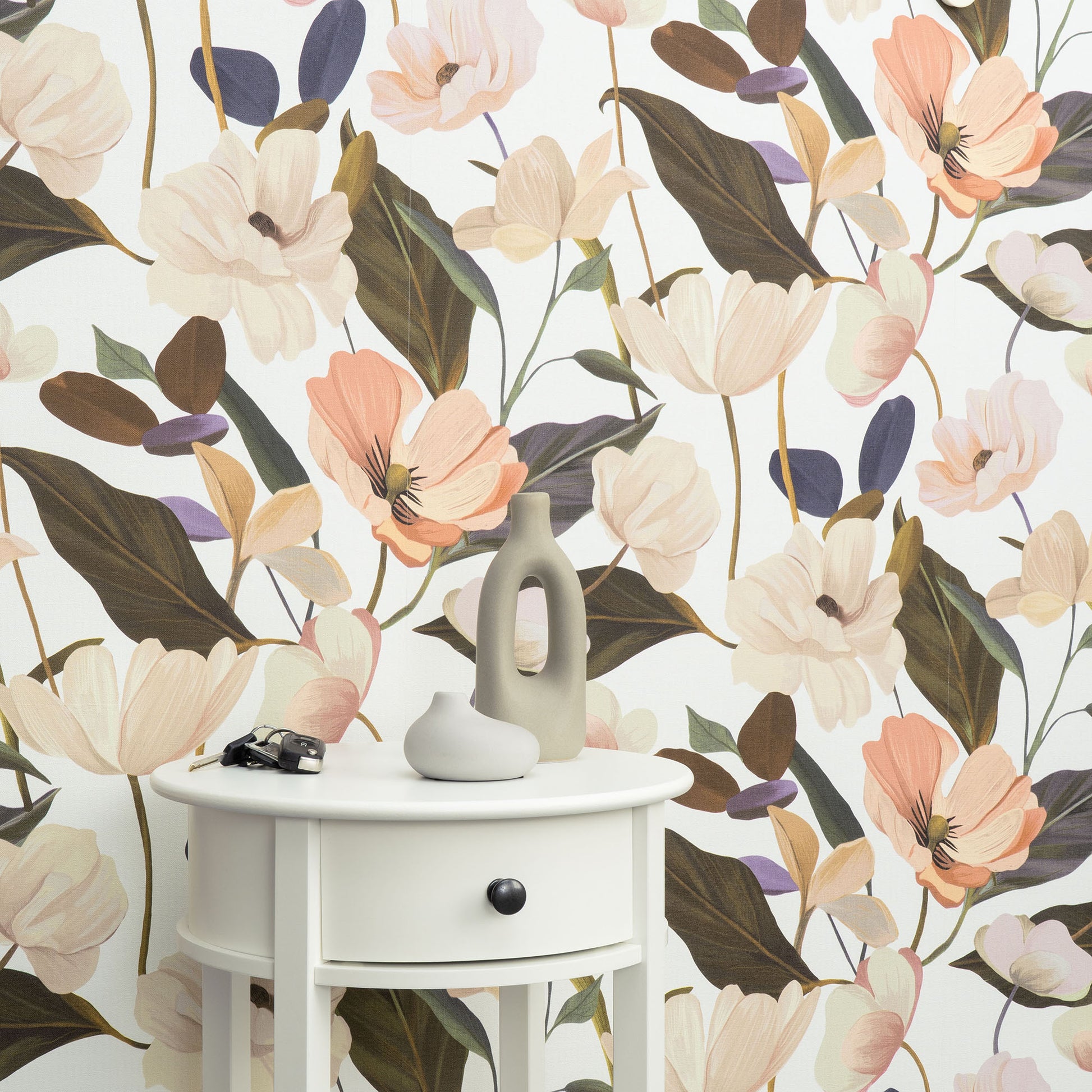 Pastel floral Fairy Blossom Pink wallpaper in the background, with a white round side table (one drawer, black knob), a grey vase and small decor in the foreground.