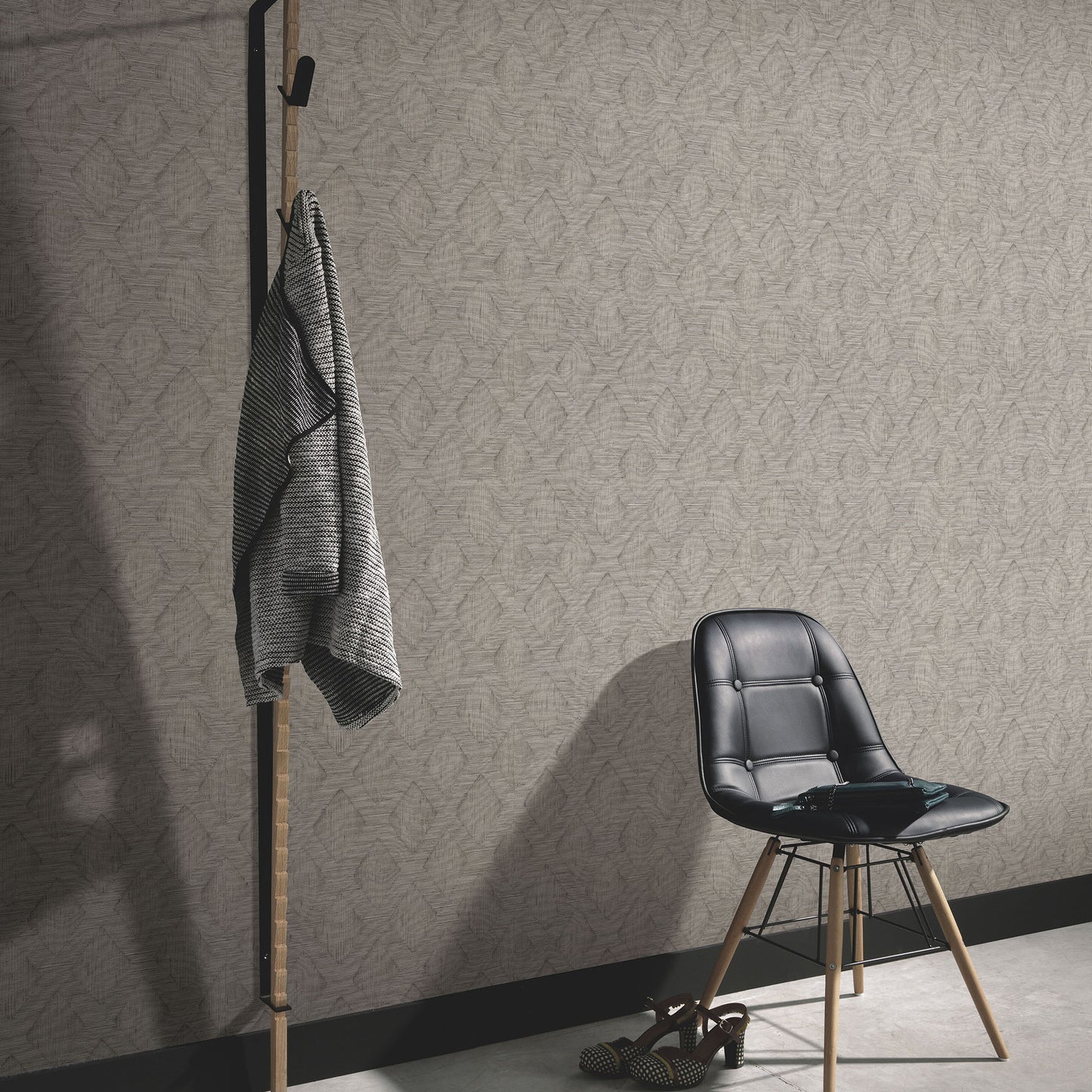 Black metal and wood coat rack with gray striped throw beside a black chair with wooden legs in a beige patterned room.