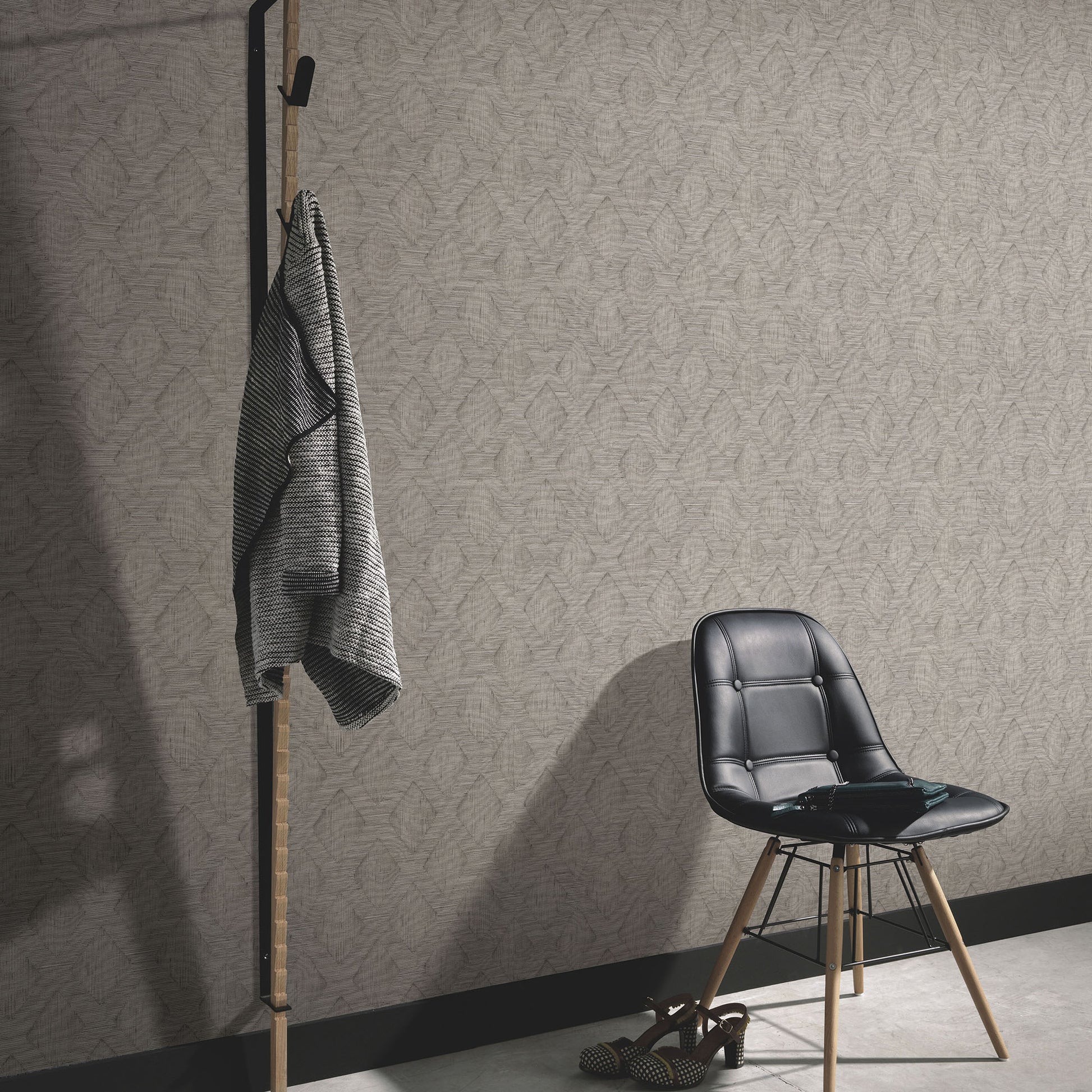 Black metal and wood coat rack with gray striped throw beside a black chair with wooden legs in a beige patterned room.