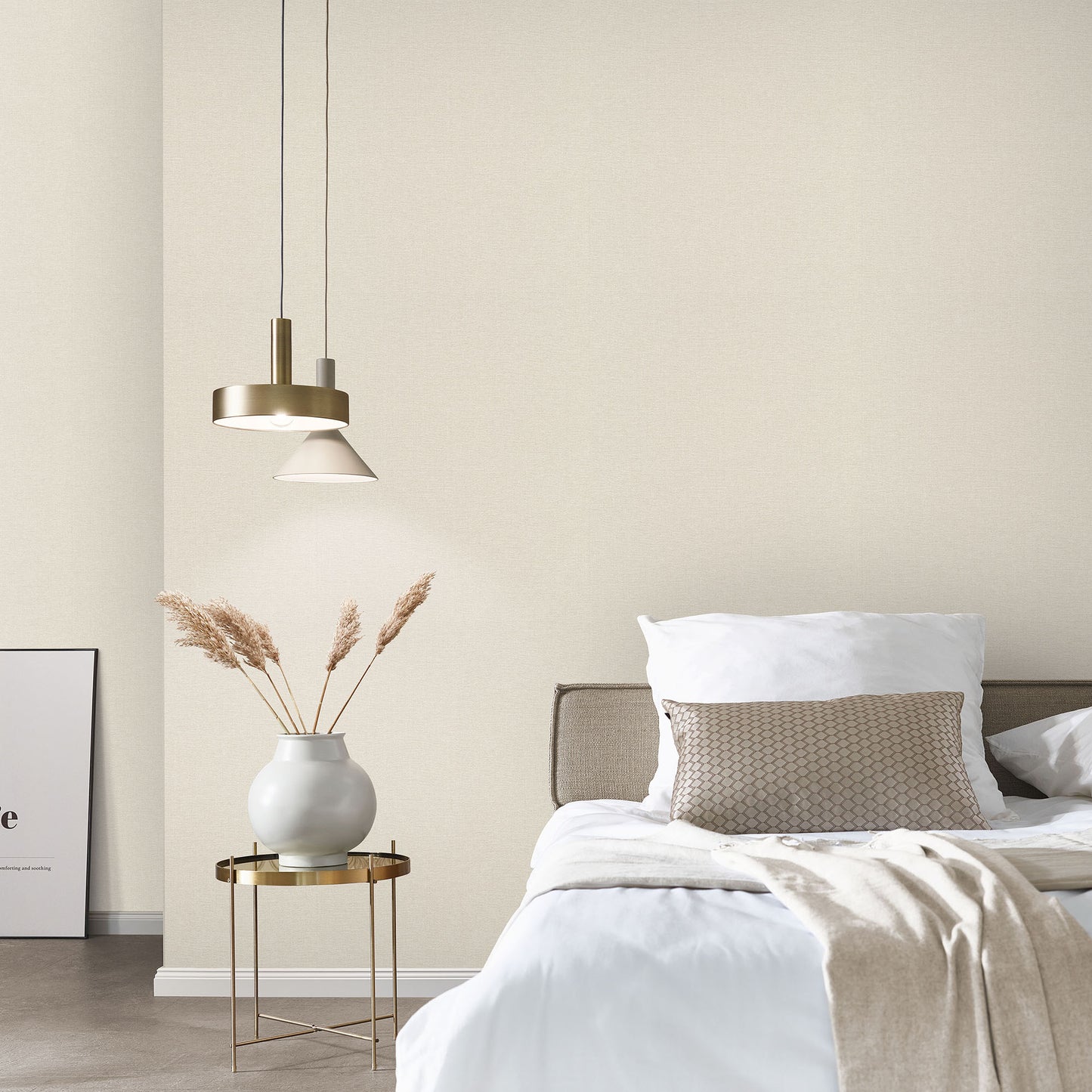Bedroom with beige linen-textured wallpaper on the walls behind white bedding; beige throw, gold side table with a white vase and dried grasses, and a brass pendant light.