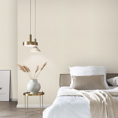 Bedroom with beige linen-textured wallpaper on the walls behind white bedding; beige throw, gold side table with a white vase and dried grasses, and a brass pendant light.
