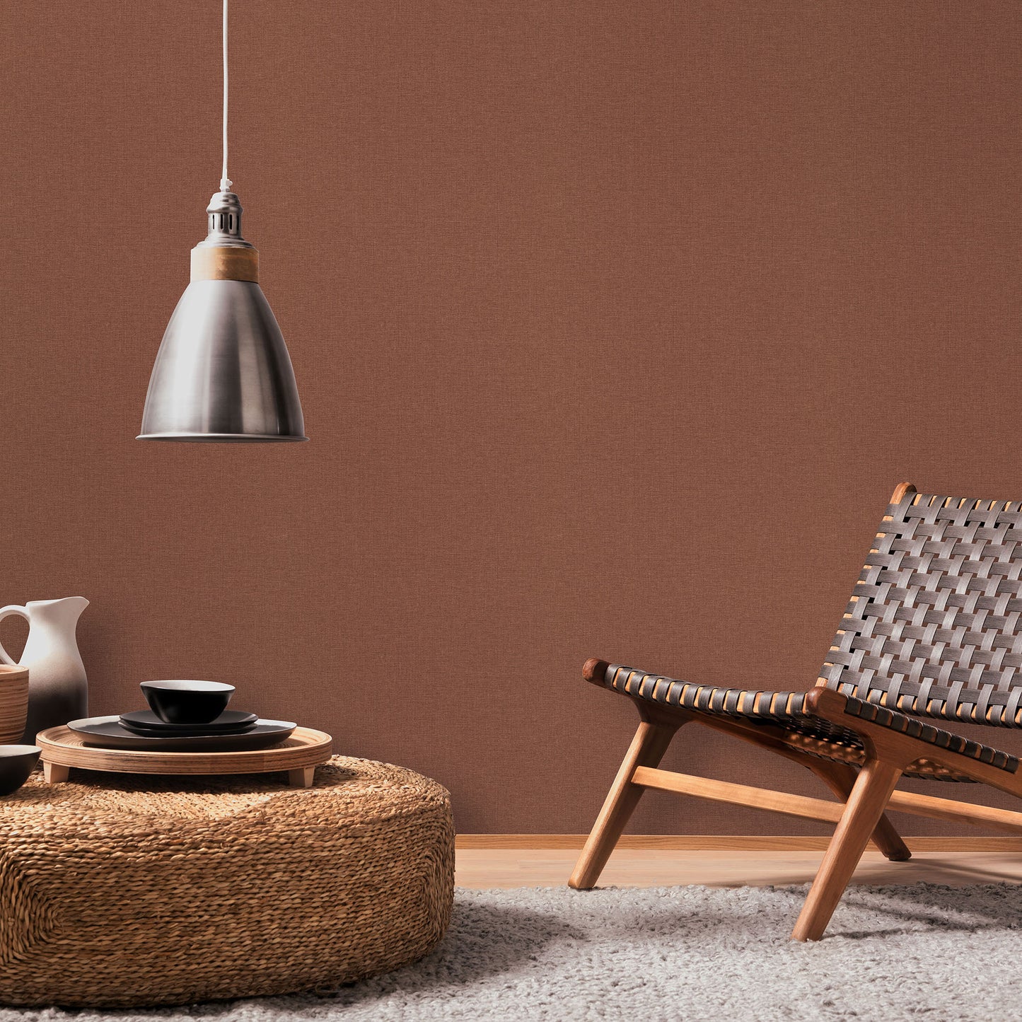 Red wallpaper pattern on a wall in a mid-century living space, with a woven lounge chair, round wicker coffee table, black dishware, and a metal pendant lamp.