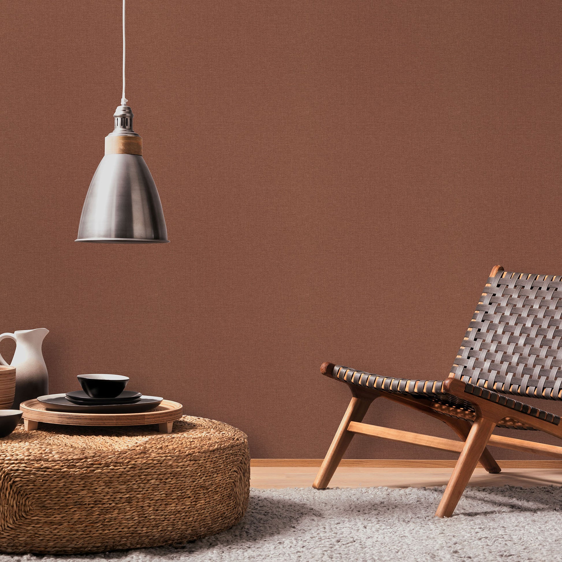 Red wallpaper pattern on a wall in a mid-century living space, with a woven lounge chair, round wicker coffee table, black dishware, and a metal pendant lamp.
