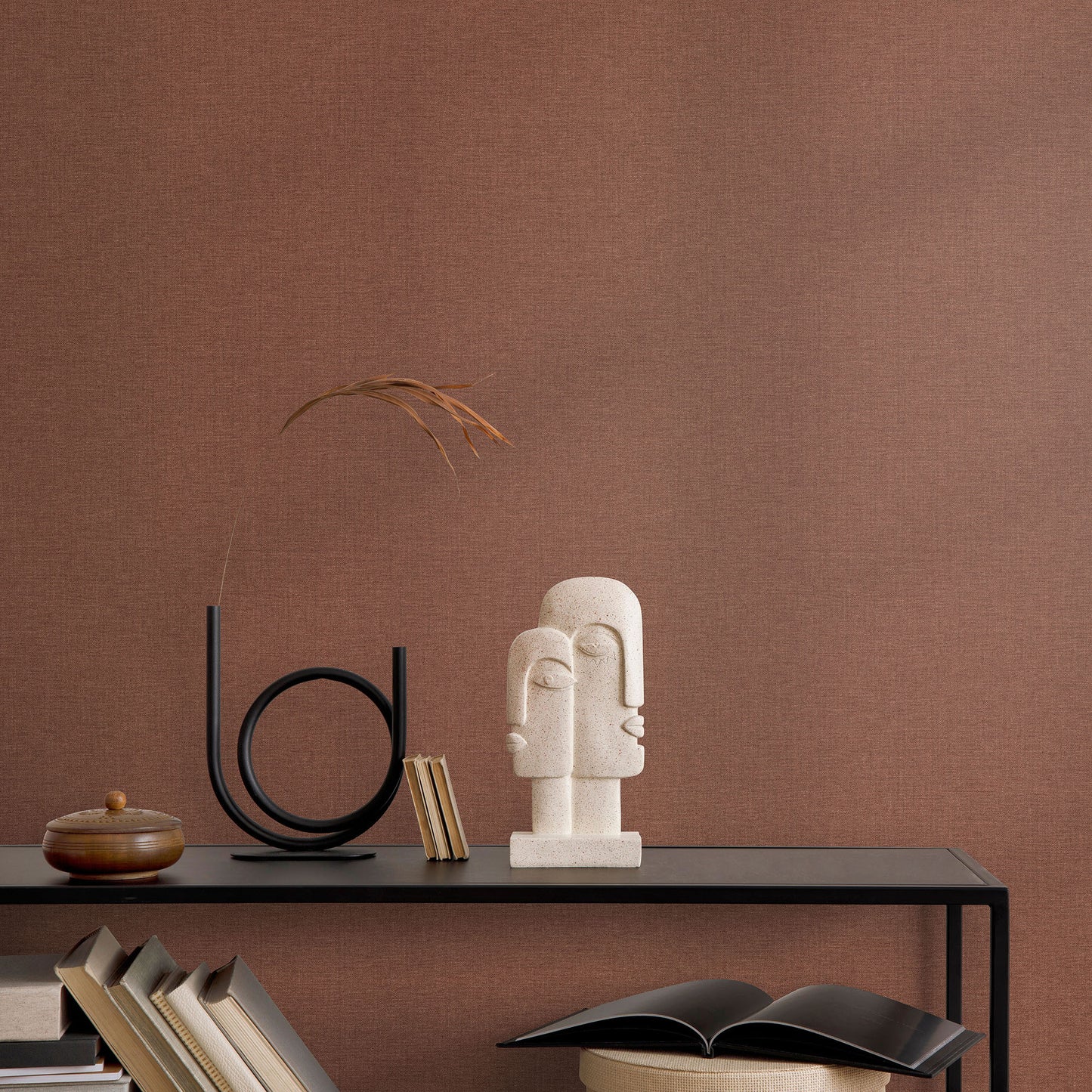 Red wallpaper backdrop for a minimalist console vignette with a beige abstract bust sculpture, circular metal sculpture, and dried grass.