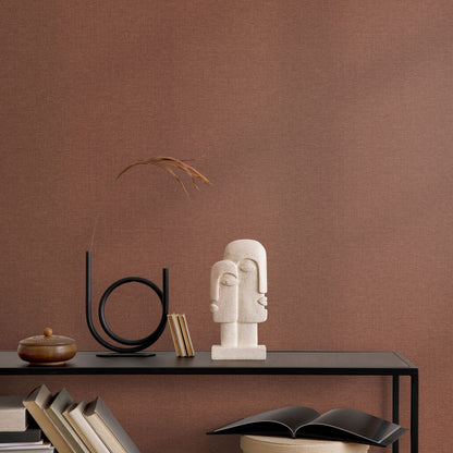 Red wallpaper backdrop for a minimalist console vignette with a beige abstract bust sculpture, circular metal sculpture, and dried grass.