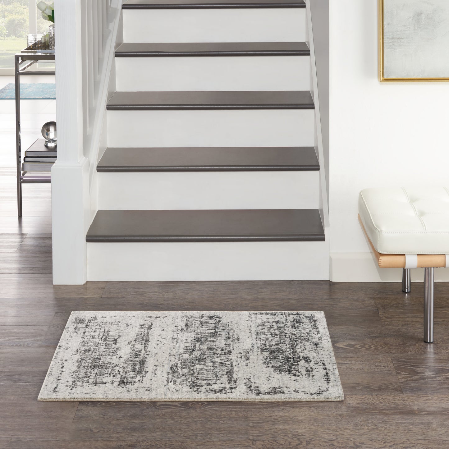 Modern staircase with dark gray treads and white risers, gray patterned rug, wood floor, and a white bench with chrome legs.