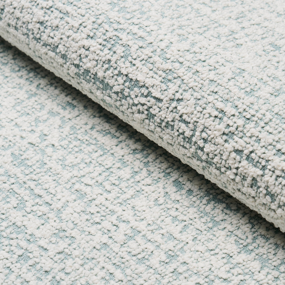 Rolled light blue-gray loop-pile rug with speckled texture, soft home decor carpet.