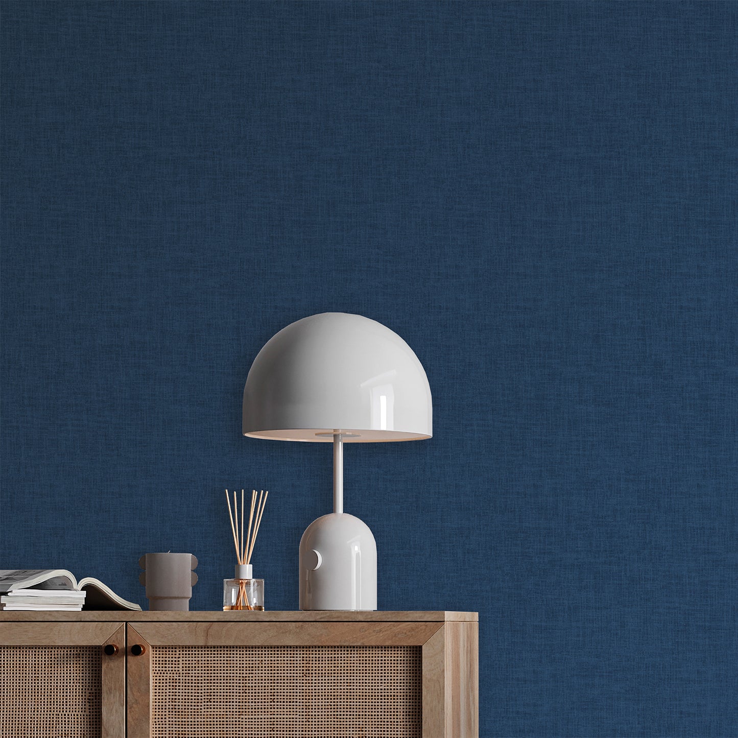 White glossy dome table lamp with curved stem on a wooden sideboard against a blue textured wall, diffuser sticks and books.