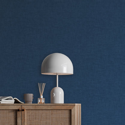 White glossy dome table lamp with curved stem on a wooden sideboard against a blue textured wall, diffuser sticks and books.