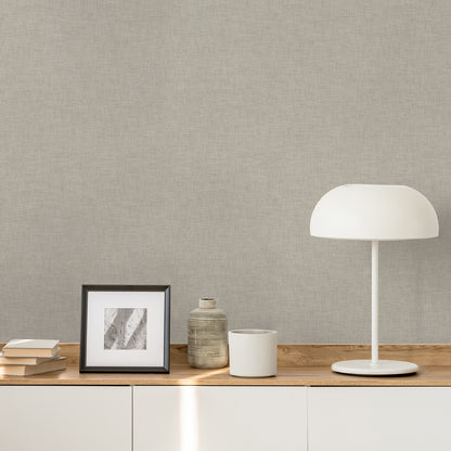 Taupe linen-weave textured wallpaper on a wall, with a wooden console, framed grayscale artwork, ceramic jar, white mug, books, and a white dome lamp.