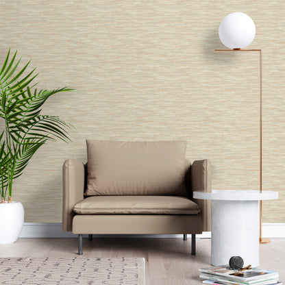 Beige armchair in a room with textured wallpaper, tall copper floor lamp, round marble side table, and a potted plant.