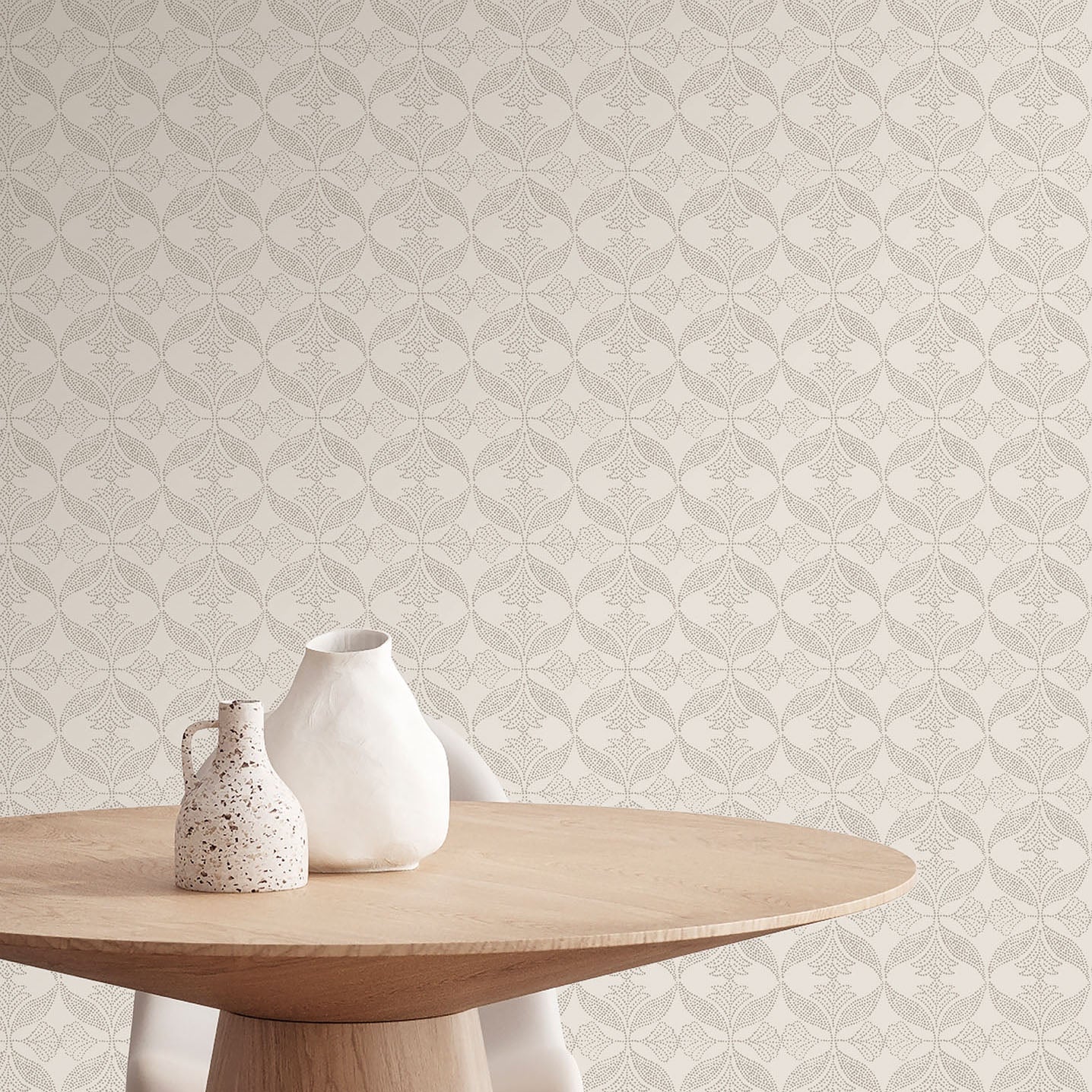Two cream ceramic vases, one speckled, on a round wooden table with beige damask wallpaper.