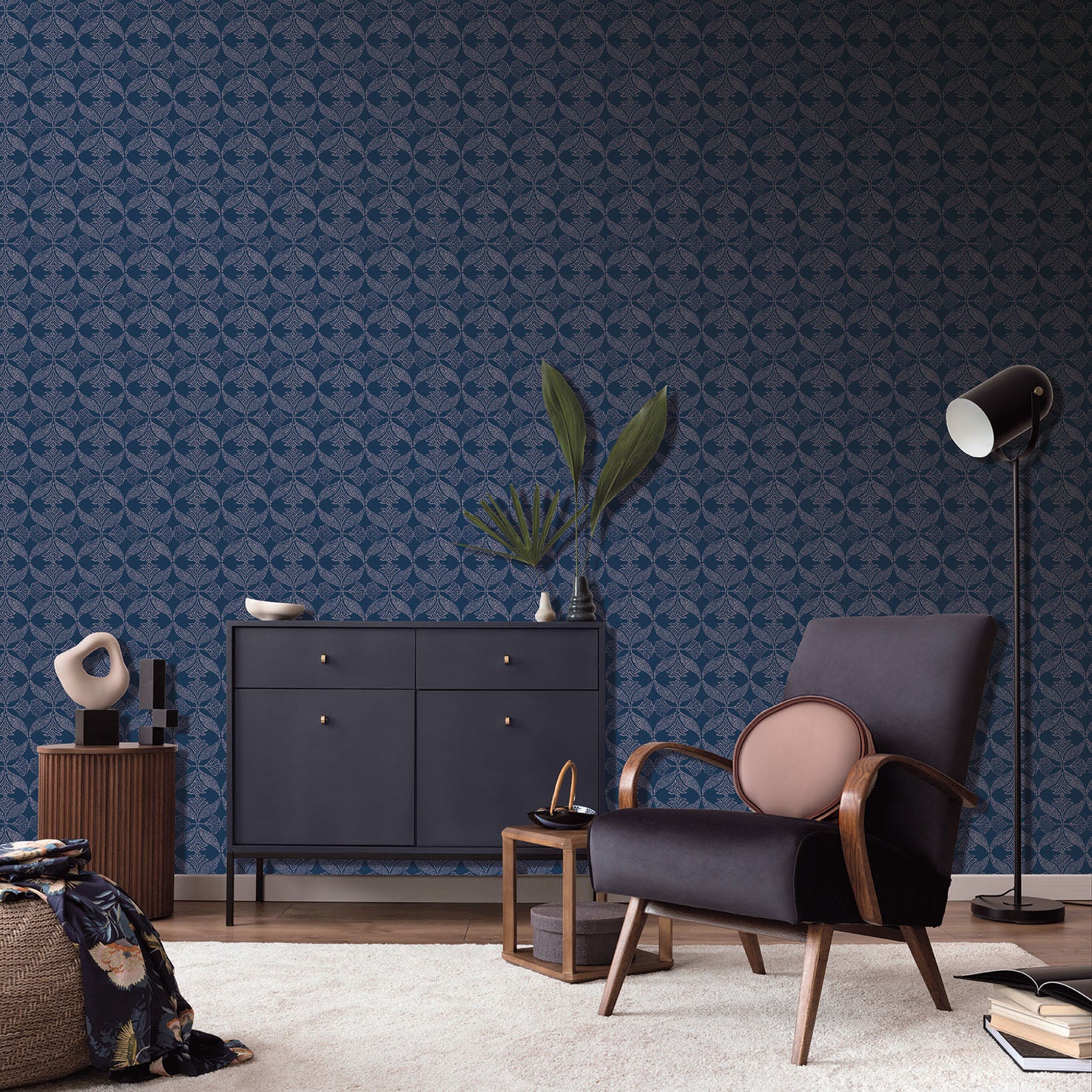 Mid-century navy armchair with wooden arms beside a navy sideboard, plant, & tall floor lamp against blue wallpaper.