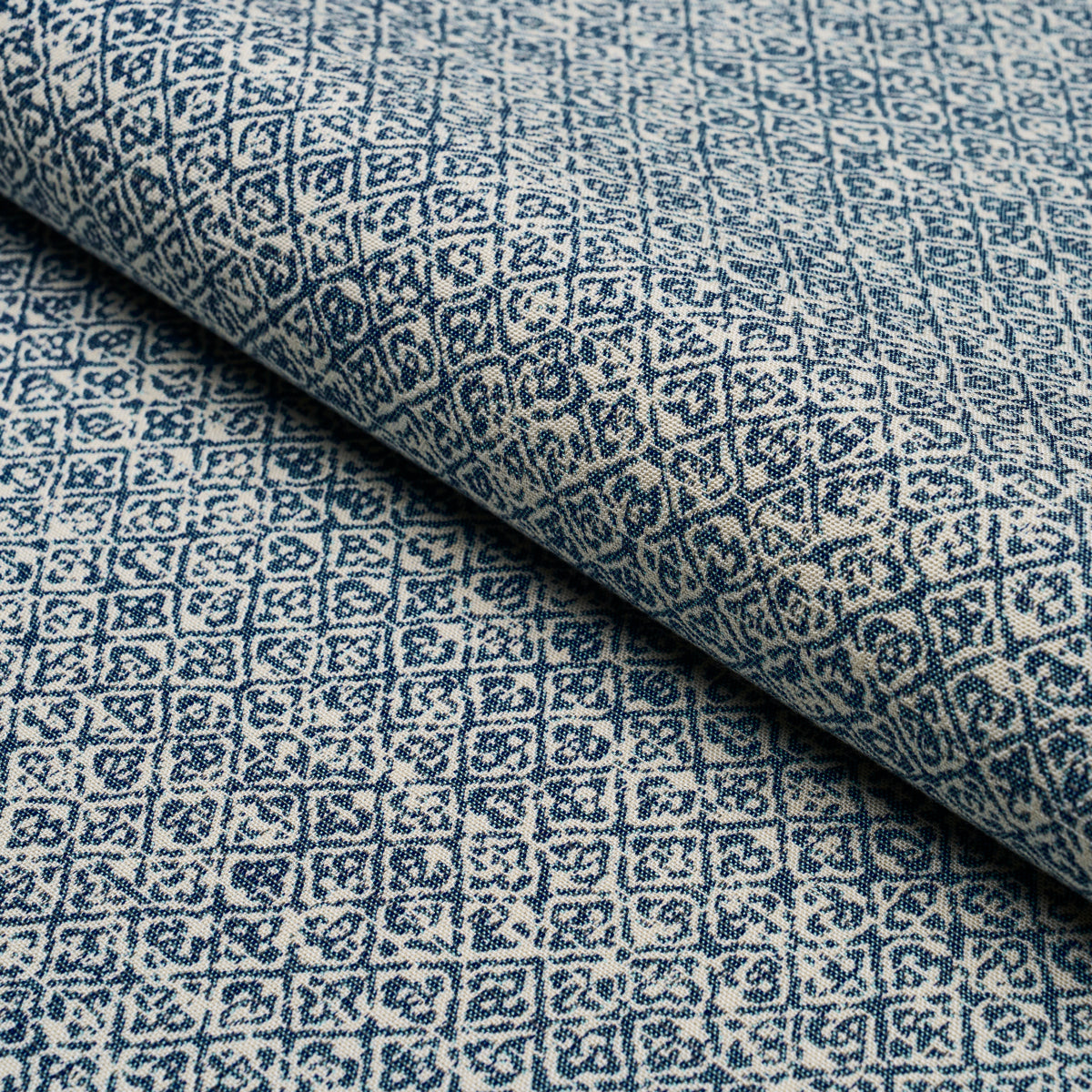 Rolled blue & white geometric patterned fabric with a diamond motif and woven texture, suitable for upholstery or drapery.