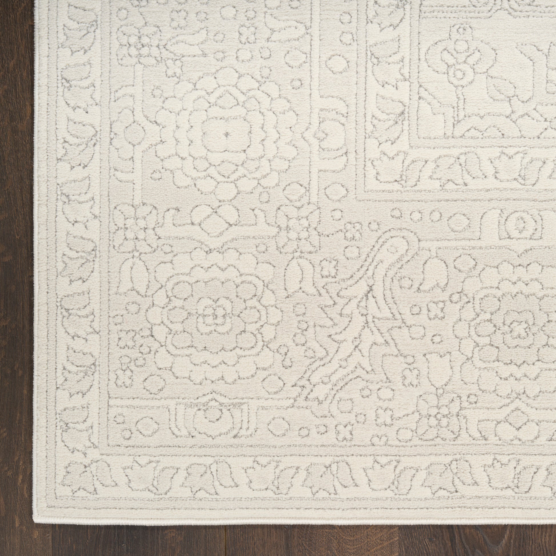 Cream ivory rectangular area rug with tonal floral medallions and ornate border on dark wood floor.