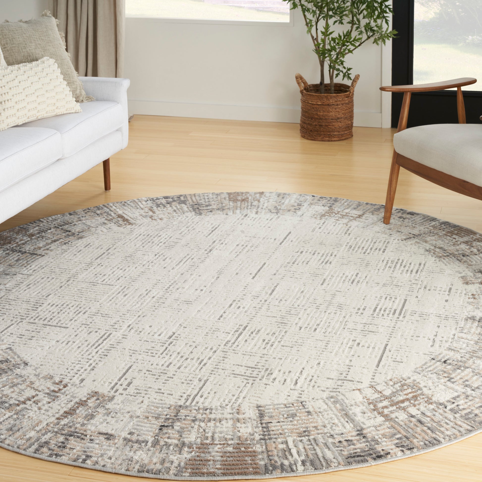 Circular rug with muted gray-beige pattern; modern living room with white sofa, wooden chair, and plant.