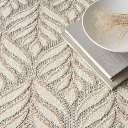 Textured cream-beige geometric rug with leaf motif; gray books and white bowl with dried grass decorative setting.